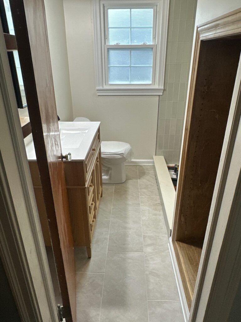 Nearly finished bathroom remodeling by Browning Craftsman Services, seen through the doorway, with a light-oak vanity, new fixtures, large-format gray floor tile, and sage wall tile