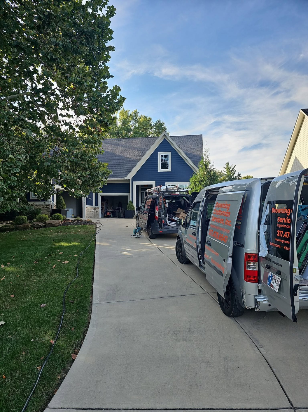 Both Browning Craftsman Services vans backed into a client's driveway, doors open, with work underway in front of a blue house