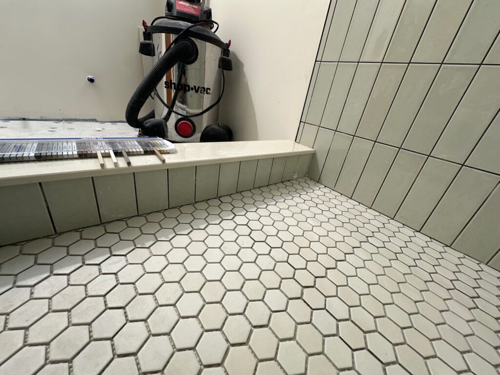 Bathroom tile installation by Browning Craftsman Services, with a white hex tile floor, sage-green vertical wall tile, and a tiled bench