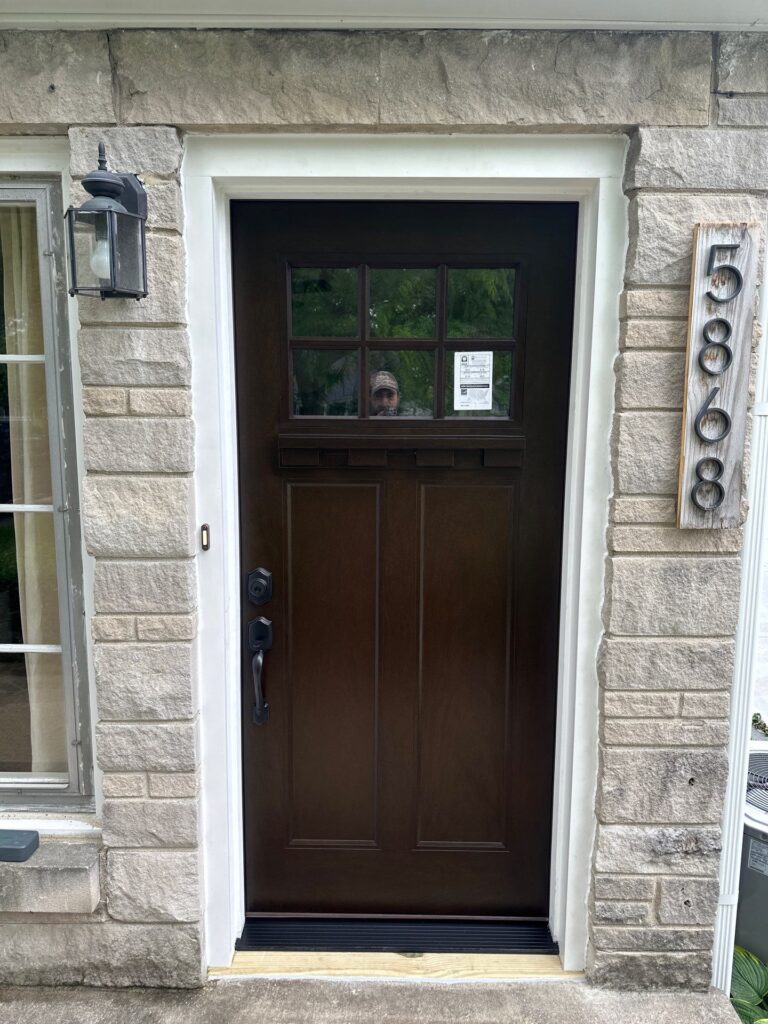 Newly installed dark walnut fiberglass front door with a six-lite window in a stone facade by Browning Craftsman Services