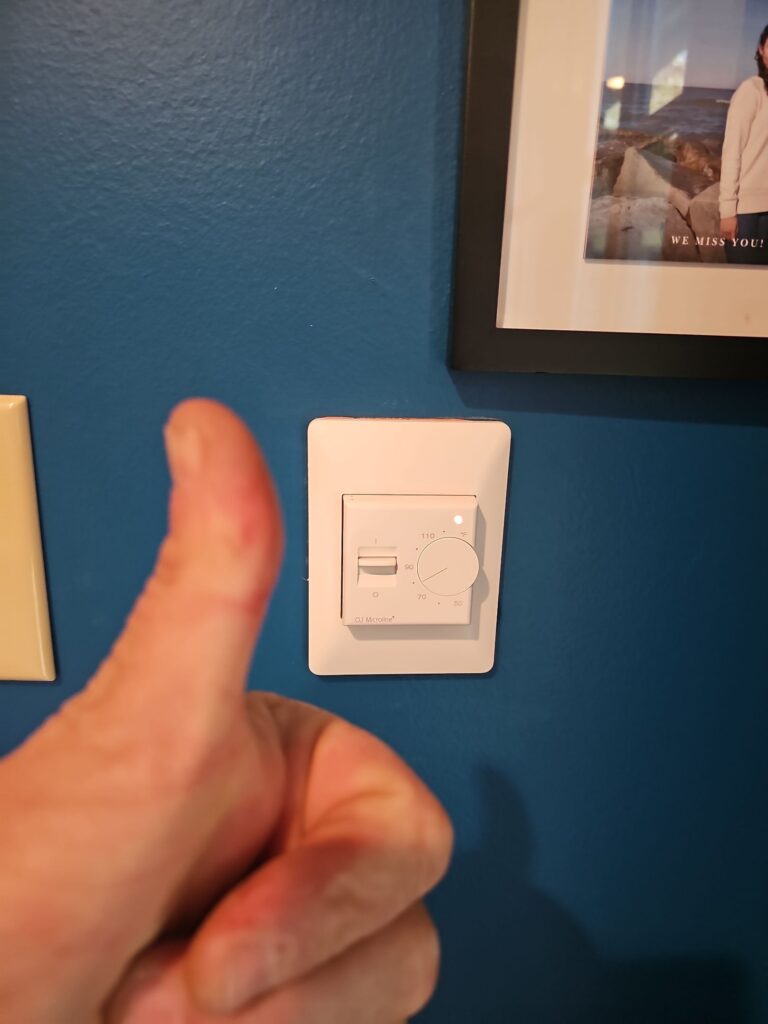 Newly installed heated-floor thermostat on a blue wall, with a technician giving a thumbs-up in the foreground, by Browning Craftsman Services